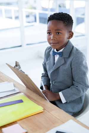 Thoughtful businessman sitting on chair by desk in officeの写真素材