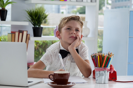 Thoughtful businessman with hand on chin sitting at desk in officeの写真素材