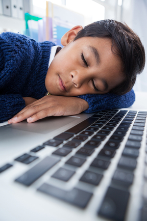 Close up of boy imitating as businessman sleeping on laptop at desk in officceの写真素材