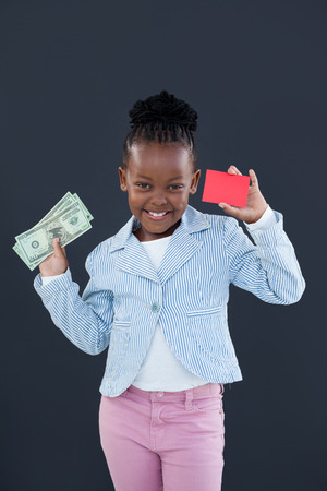 Portrait of businesswoman holding red card and paper currency while standing against gray wallの写真素材