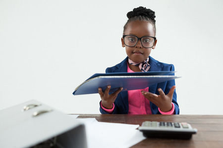Portrait of businesswoman wearing eyeglasses holding file while sitting at desk in officeの写真素材