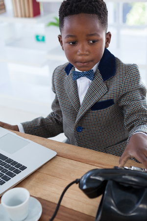 Serious businessman with telephone and laptop sitting at desk in officeの写真素材