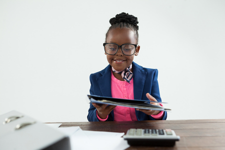 Smiling businesswoman wearing eyeglasses holding file while sitting at desk in officeの写真素材