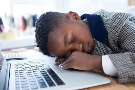 Businessman taking a nap on laptop at desk in officeの写真素材