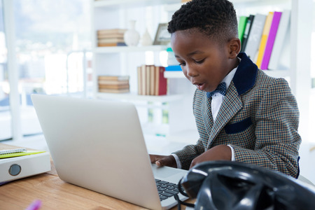 Businessman using laptop at desk by bookshelf in officeの写真素材
