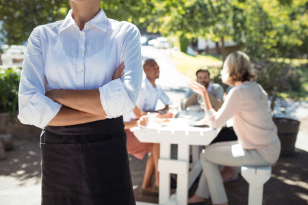 Mid section of waitress standing with arms crossed in restaurantの写真素材