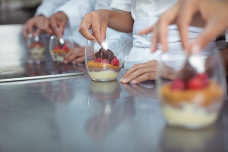 Mid-section of chefs finishing dessert in glass at restaurantの写真素材
