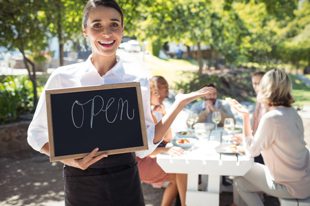 Smiling waitress standing with open sign board in restaurant