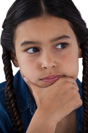 Close-up of thoughtful girl with hand on chin against white backgroundの写真素材