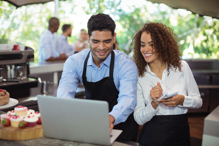 Male waiter and female waitress with laptop at outdoor restaurantの写真素材