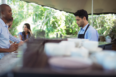 Male waiter taking order at counter in outdoor cafeの写真素材