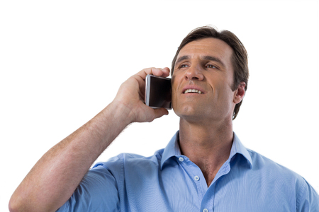 Male executive talking on mobile phone against white backgroundの写真素材