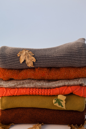 Stack of woolen clothing with autumn leaves against white backgroundの写真素材
