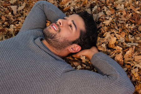 Thoughtful man lying on autumn leavesの写真素材