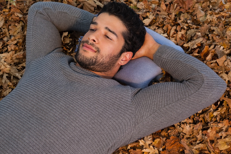 Thoughtful man lying on autumn leavesの写真素材