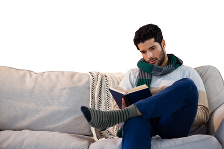 Man sitting on sofa while reading book against white backgroundの写真素材