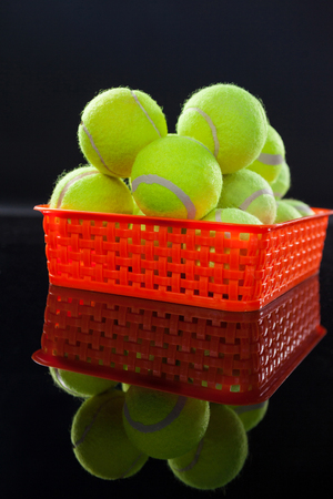 Close up of tennis balls in red plastic basket with reflection against black backgroundの写真素材
