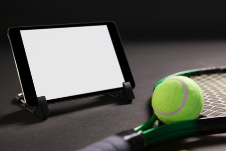 Close up of digital tablet by tennis racket and ball on black backgroundの写真素材