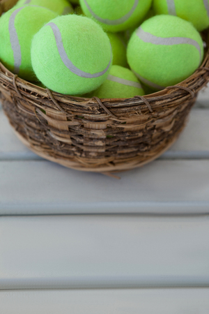 High angle view of fluorescent yellow tennis balls in wicker basket on white wooden tableの写真素材