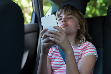 Attentive teenage girl using mobile phone in the back seat of carの写真素材
