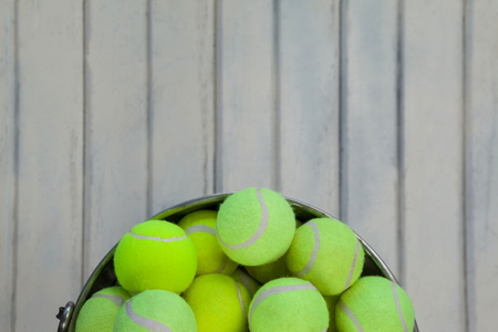 Directly above view of fluorescent yellow tennis balls in metallic bucket on white wooden tableの写真素材