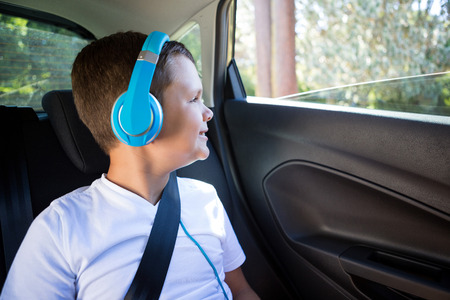 Smiling teenage boy with headphones sitting in the back seat of carの写真素材