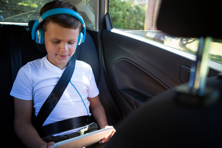 Attentive teenage boy using digital tablet in the back seat of carの写真素材