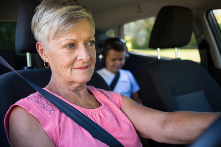 Grandmother driving a car while grandson sitting in the back seat of car