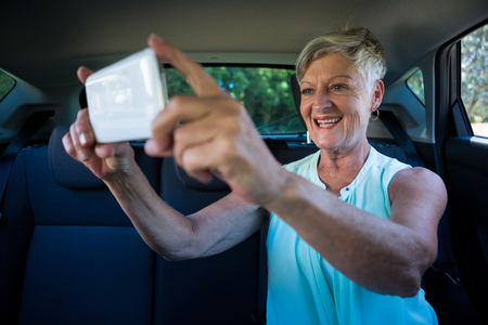 Senior woman taking selfie on mobile phone in carの写真素材
