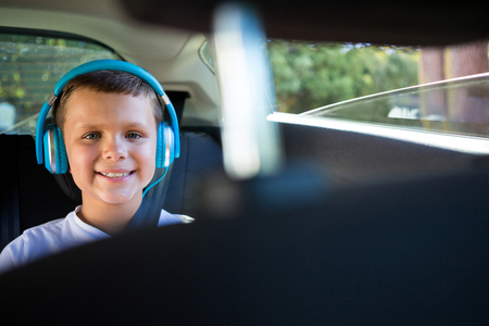 Portrait of smiling teenage boy with headphones sitting in the back seat of carの写真素材