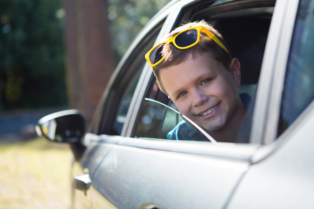 Teenage boy looking from open car window on a sunny dayの写真素材