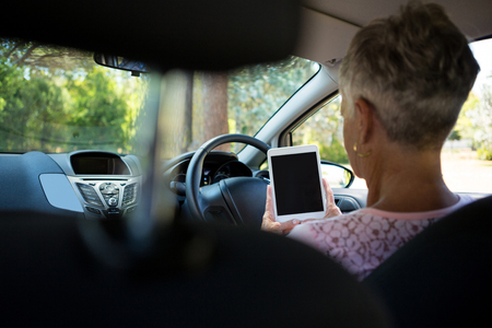 Rear view of senior woman using digital tablet while driving a carの写真素材