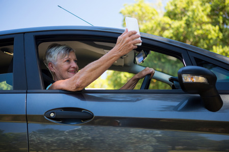 Senior woman taking selfie with mobile phone in a carの写真素材