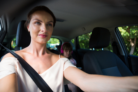 Happy woman driving a car while daughter sitting in the backseat of carの写真素材