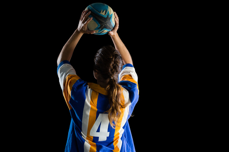 Rear view of female athlete playing rugby against black backgroundの写真素材