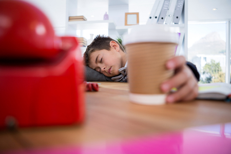 Boy as business executive sleeping while holding coffee cup in officeの写真素材
