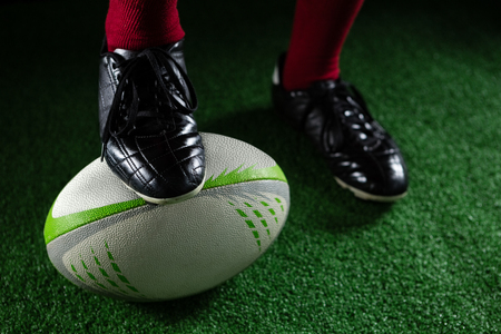 Low section of sportsperson stepping on rugby ball while plying rugbyの写真素材