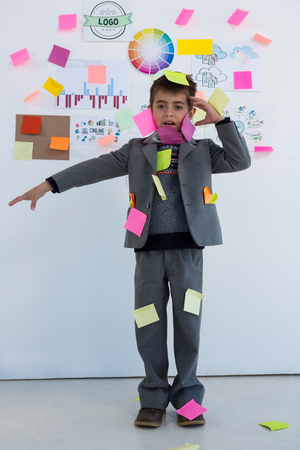 Boy as business executive with sticky notes on his body in officeの写真素材