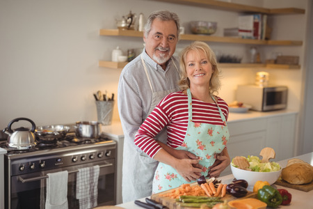 Portrait of smiling senior couple embracing each other in kitchen at homeの写真素材