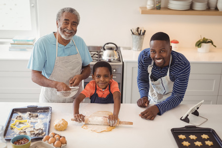 Boy preparing cookie dough with his father and grandfather in kitchen at home