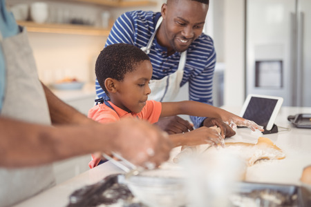 Boy preparing cookie dough with his father and grandfather in kitchen at homeの写真素材