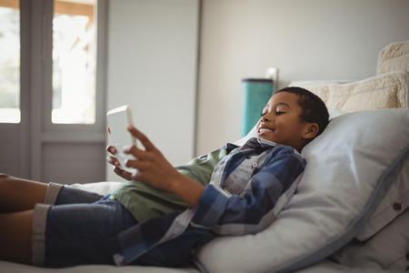 Smiling boy using digital tablet while lying on bed in bedroomの写真素材