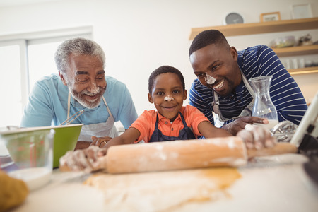 Boy preparing cookie dough with his father and grandfather in kitchen at homeの写真素材