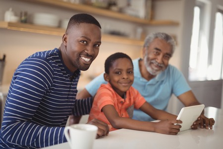 Portrait of happy multi-generation family using digital tablet in kitchen at home