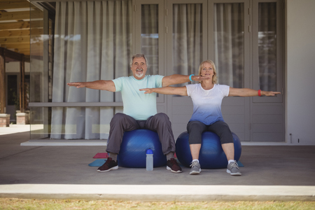 Senior couple doing stretching exercise on exercise ball at verandaの写真素材