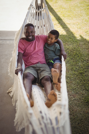 Portrait of smiling father and son relaxing on a hammock in gardenの写真素材