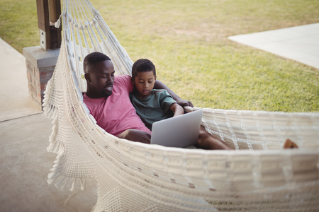 Father and son using laptop while relaxing on a hammock in gardenの写真素材