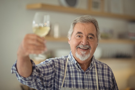 Portrait of senior man holding a glass of wine at homeの写真素材