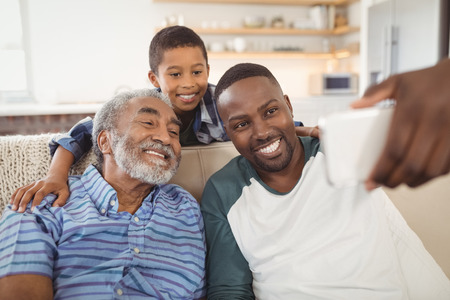 Smiling multi-generation family taking selfie from mobile phone in living room at homeの写真素材
