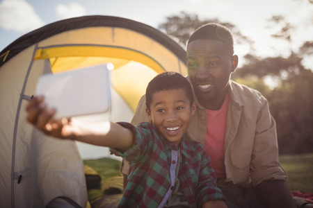 Smiling father and son taking selfie with mobile phone in parkの写真素材